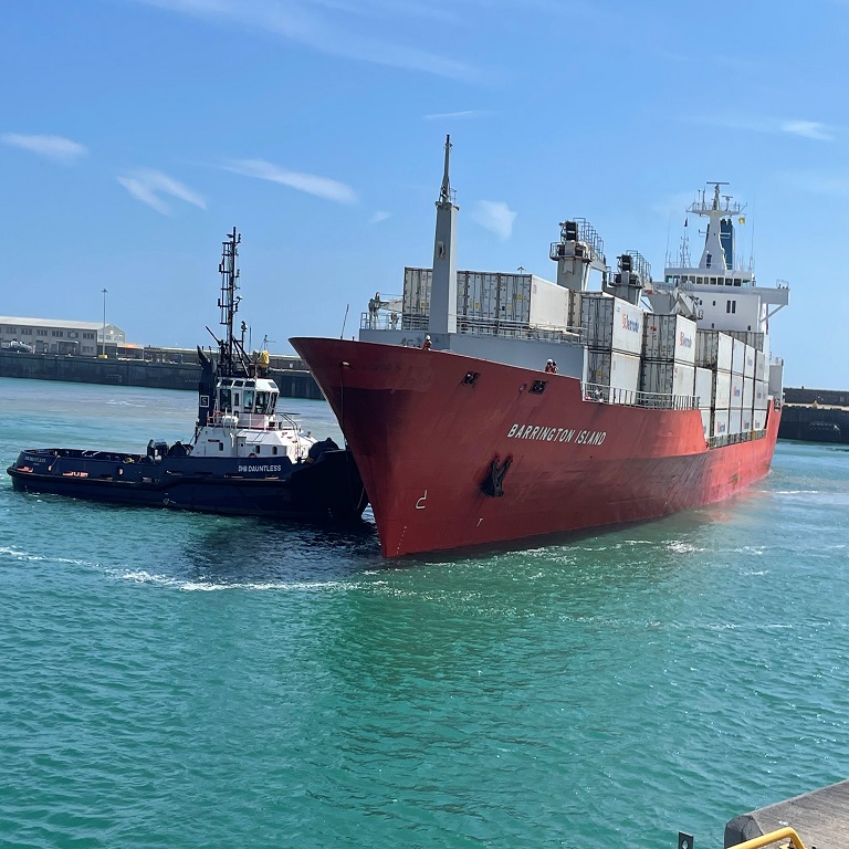 Cargo vessel Barrington Island loaded with containers of fruit berthing at Dover Cargo Terminal with a tug assisting.