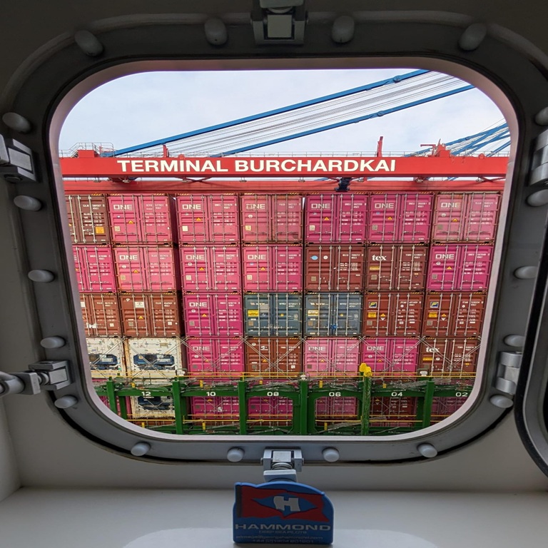 View of stacked containers through port hole window of container ship
