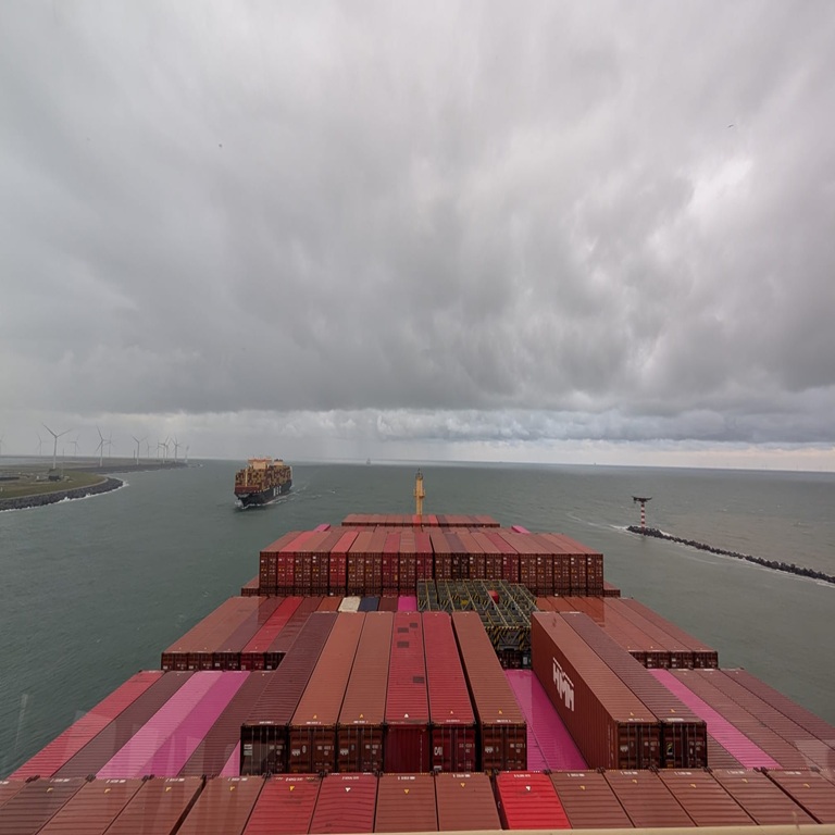 View of containers stretching out on deck of container ship at sea with land in background